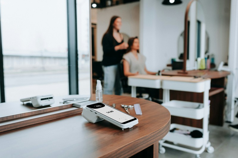 Salon scene showing a haircut in progress with a card reader visible at the station
