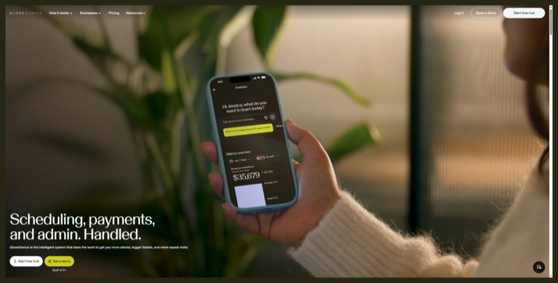GlossGenius homepage, headline "Scheduling, payments, and admin. Handled." beside a hand holding a phone showing a revenue dashboard