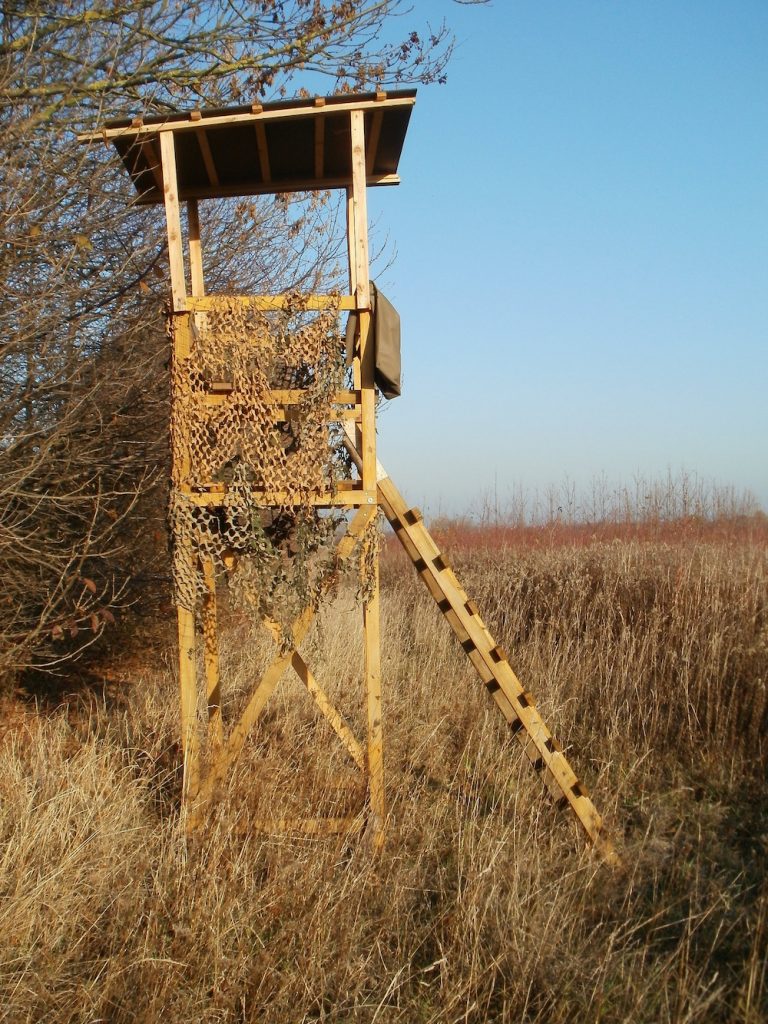 A free-standing deer stand is on the edge of a prairie.