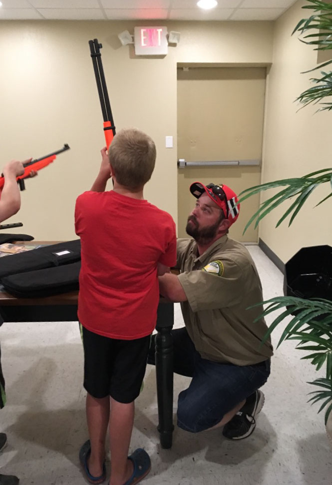 A hunter safety teacher helps a student safely hold a firearm.