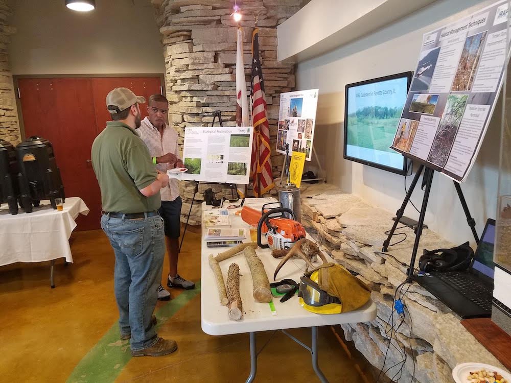 Two people converse in front of an informational poster and a table with various object relating to habitat restoration and conservation.
