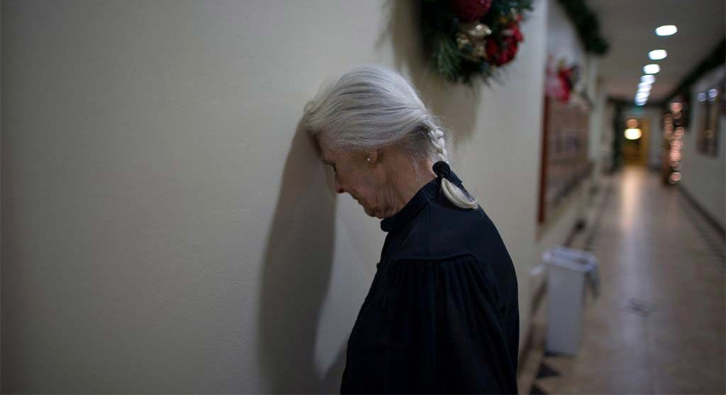 still from 'Familiar Touch' showing an older woman (Ruth, played by Kathleen Chalfant) standing in a hallway with her head against the wall