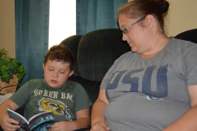 Brayden Borger reads aloud to his mother, Jennifer, from one of his favorite books, "I Survived the Japanese Tsunami, 2011," by Lauren Tarshis. Brayden must read for a half-hour each day and work in his math and writing workbooks to help him retain…