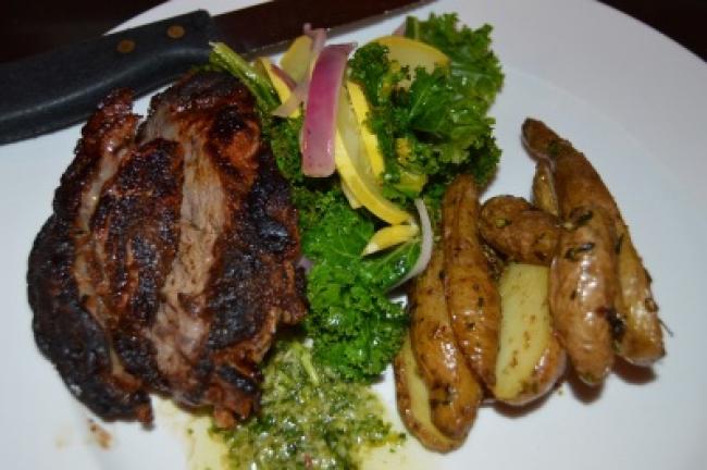 Sliced steak with Chimichurri sauce, and a side of fingerling potatoes and vegetables.