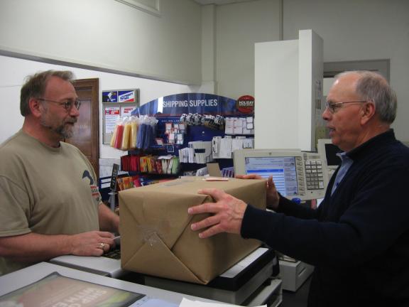 STACEY SOLT/TIMES NEWS Jim Strubinger, right, helps customer Kenneth Straub of Weissport weigh a package for shipping at the Lehighton Post Office. The United States Post Office is encouraging customers to take care while shipping and labeling…