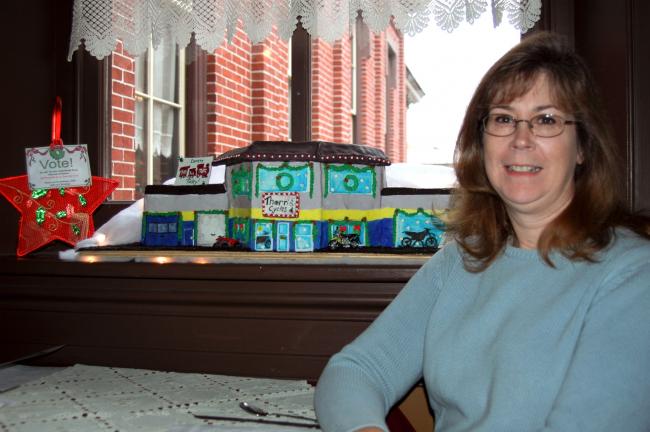 Sheryl Beltz, Barnesville, started a tradition five years ago by establishing a gingerbread house contest to benefit the U. S. Marine Corps League's Toys for Tots program. Here, Beltz poses with one of this year's entries, a model of Thorn's Cycle…