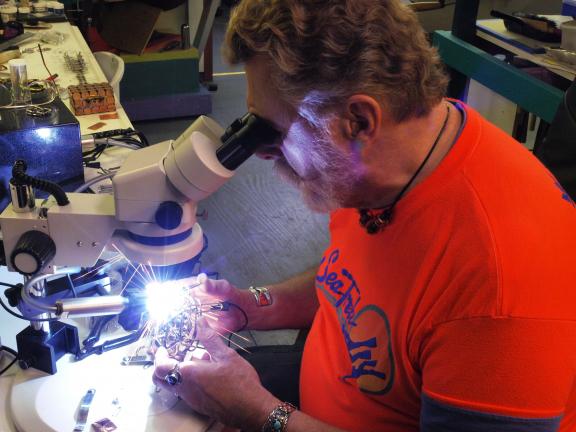 AL ZAGOFSKY/SPECIAL TO THE TIMES NEWS Using a stereo microscope, Nic East welds a piece of three-dimensional scroll-designed jewelry using a micro-welder at his Jim Thorpe studio. With a growing popularity for their Southwestern-styled jewelry using…