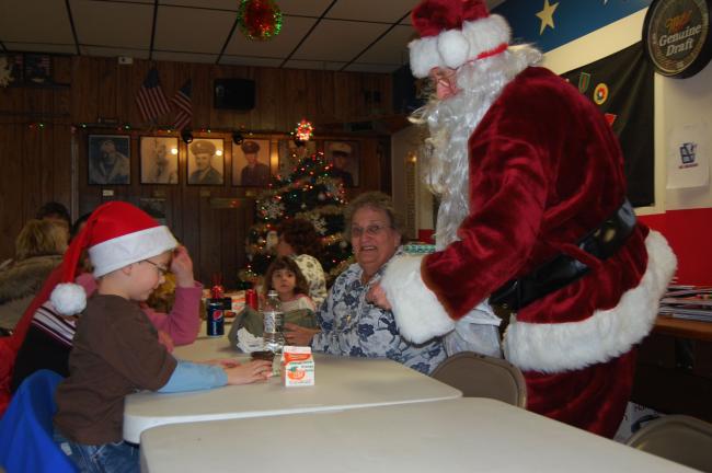 Two Santas meet across the table as Skylar Green dons his hat.
