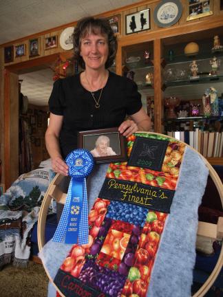 AL ZAGOFSKY/SPECIAL TO THE TIMES NEWS Kathy Long with a photo of her late mother, Grace Rhoads, her mother's blue ribbon from the 2009 Carbon County Fair, and her mother's winning quilt patch that Long is reworking into a wall hanging to be donated…