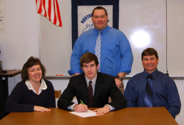 TJ ENGLE/TIMES NEWS Northern Lehigh's Jake Kern signs a letter of intent to continue his academic and athletic career at Colgate University. With Kern are his parents, Laura and Steve. Standing is Bulldog head football coach Joe Tout.