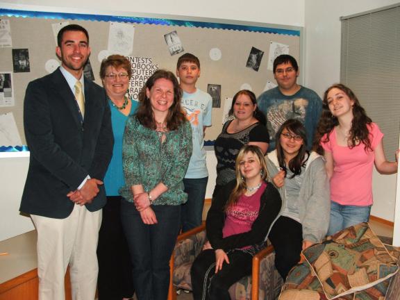 @$:MICHAEL HEERY/SPECIAL TO THE TIMES NEWS In celebration of School Library Month and National Library Week, Lehighton Area High School recently hosted a "Library Tea." Pictured, from left, in front of a billboard that was designed by the students…