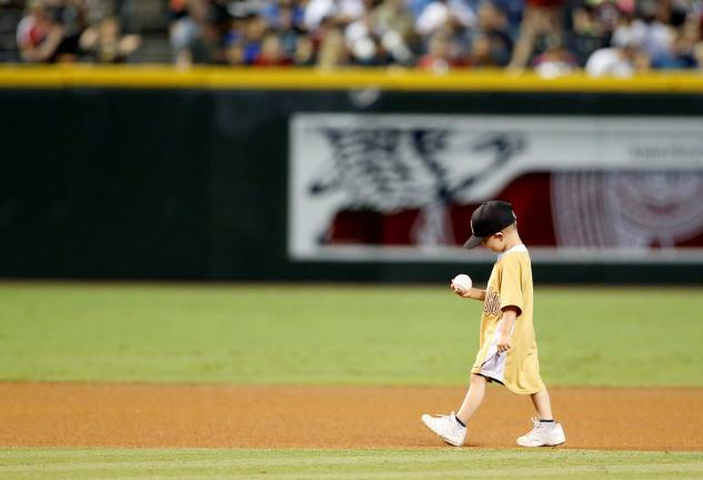A youngster who's battled cancer smiles as he walks off the field with an autographed baseball from a Arizona Diamondback before the Diamondbacks game with the San Diego Padres, Saturday, Sept. 13, 2014, in Phoenix. (AP Photo/Darryl Webb)
