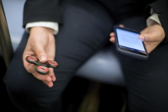 FILE - In this May 10, 2017 file photo, attorney Kim Juszczak uses a fidget spinner while riding the subway in New York. Fidget spinners are among the those on the annual list of hazardous summer toys compiled by World Against Toys Causing Harm, Inc…
