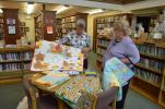 Diane Danielson, left, and Terri Sheckler look at the quilts, afghans and pillowcases that will be donated to Project Linus and Turning Point of Lehigh Valley. Below, Danielson, holds up the quilt show door prize, a quilted wall-hanging of flowers…