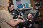 AMY MILLER/TIMES NEWS Debbie Balch, administrative assistant for Care Net of Carbon County, left, fits Bonnie Lynn Reason, 11 months, into a car seat, as her mother, Crystal Reason, of Lansford, watches. Car seats are required to keep children safe…