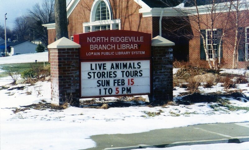 A sign outside the North Ridgeville branch announces an upcoming open house on February 15, 2004. The text of the sign reads: "Live Animals Stories Tours Sun Feb 15 1 - 5 PM".