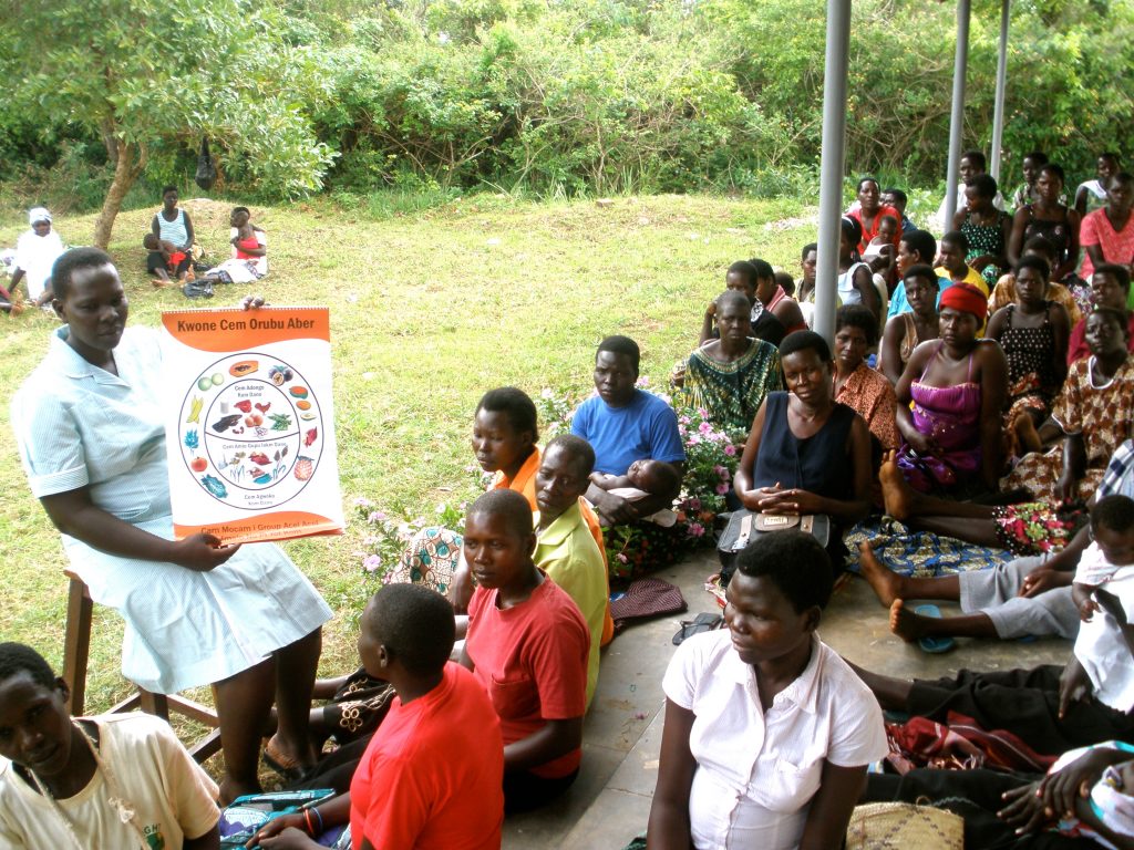 “Your child can achieve great things,” midwife Susan Ejang tells a gathering of new moms and moms-to-be at a clinic near Lira, Uganda. She is leading a nutrition class. Esther, pregnant at the time, is in the front row, wearing an orange shirt, three women to Susan’s left.