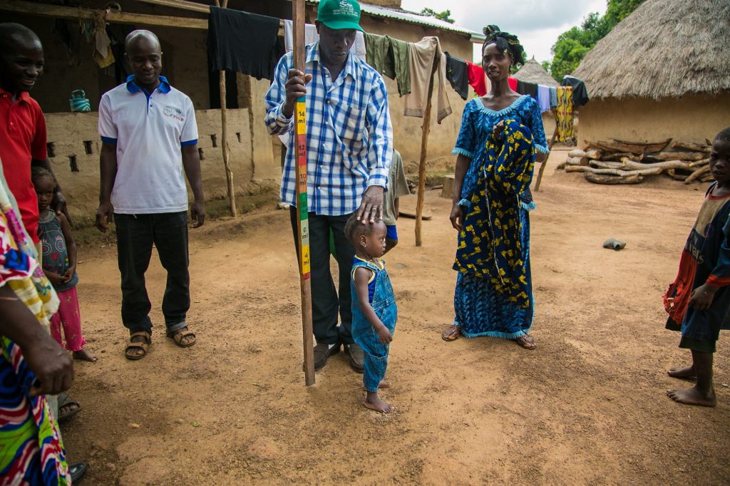Toumany Conde, community health worker, demonstrates how he would measure a child in order to determine the correct medicine dose during a mass treatment campaign.