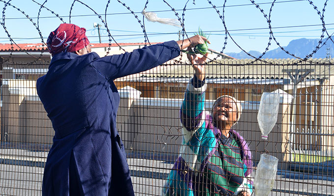 Ntombi Mbinda hands produce to a woman passing by the garden.