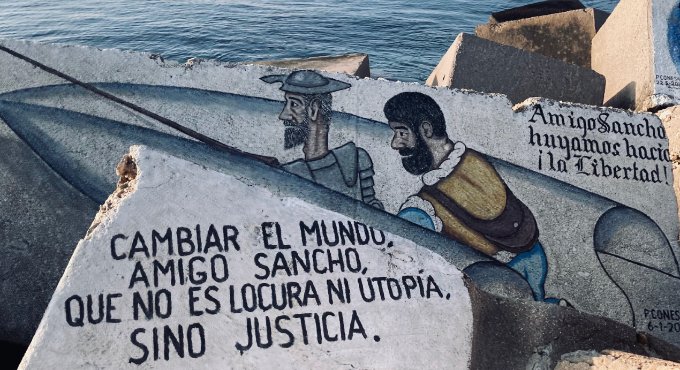 Un mur al costat del mar que té un escrit que diu: "Cambiar el mundo, amigo sancho, que no es locura ni utopía, sino justicia"