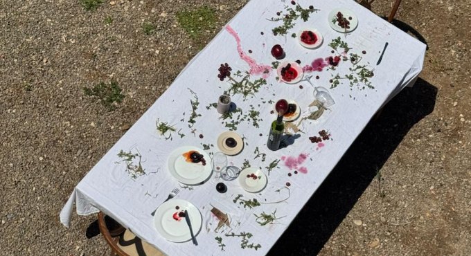Una taula llarga parada amb estovalles blanques i diverses copes de vi abocades a la taula. També hi ha plats i flors per sobre la taula. 