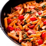 Red pesto penne pasta with chicken, spinach, baby tomatoes and onions in a large skillet.