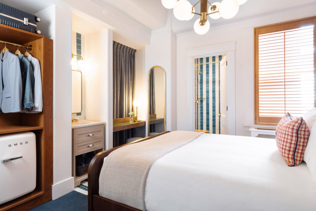 Palihotel San Diego - left to right - closet with hanging jackets and mini fridge, in-room vanity, small work desk with ottoman, view into bathroom, bed