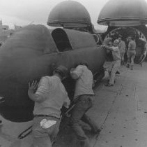 Navy men strain to move a swimmer delivery vehicle along a track