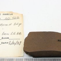 Polished adze fragment with artifact slip and ruler