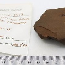 Polished basalt adze fragment with artifact slip and ruler