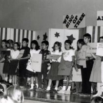 Black and white,  2.25x3.5. 5th grade student program Students are holding up signs to represent each state. Signs in background: "America" "We Sing of Thee" Byrd Elementary School. Yokohama, Japan