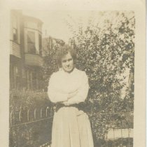(673)Gertrude Duesenberg standing by a metal fence, apartment in background