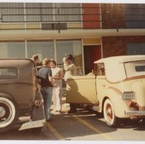 Four unidentified people in front of motel between Yellow and Brown Auburns