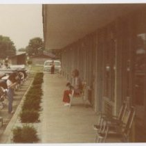 Unidentified Woman with small dog on chair in front of motel with Parking lot Right Aligned