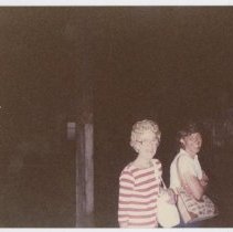 Unidentified woman with glasses wearing a red and white striped shirt stands next to another woman