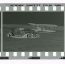 Cord L-29 Cabriolet in front of Stinson airplane out in field.