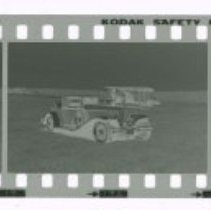 Cord L-29 Cabriolet in front of Stinson airplane out in field.