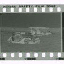 Cord L-29 Cabriolet in front of Stinson airplane out in field.