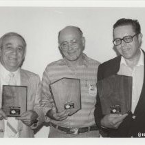 Black and white photo of three men holding ACD award plaques