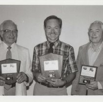 Black and white photo of three men holding ACD award plaques