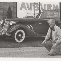 Man kneeling next to a 1936 Auburn 852 in front of the museum