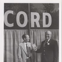 Two men holding an ACD Club award in front of the museum