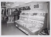 Black and white photograph of mens clothing section showing ties, shirts, a