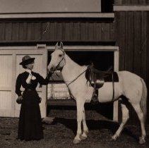 Woman holding a saddled horse.
