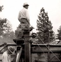 Two men filling sacks with grain from the threshing machine.