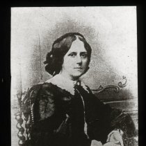 Woman posed. Her hands are together. Dress has ruffles on collar and sleeve