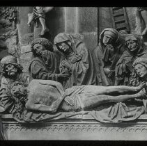 Sculpture of 6 people gathered around Jesus (maybe) as he lies down.