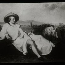 Image of a man sitting, leaning back with one of his legs sticking out. Tow