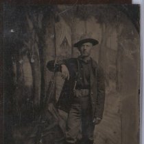 Tin type photo man in field gear next to a rifle.