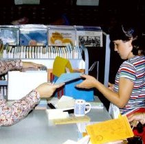 Seated adult handing a booklet to a child and an adult.